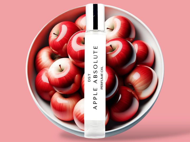 10ML bottle of Apple Absolute perfume oil sitting in front of a large white bowl filled with red apples against a light red background. 