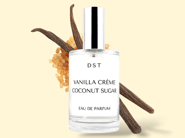 100ml bottle of Vanilla Creme and Coconut Sugar Parfum sitting in front of 2 large vanilla beans that are lying on top of a pile of brown sugar against a cream colored background. 