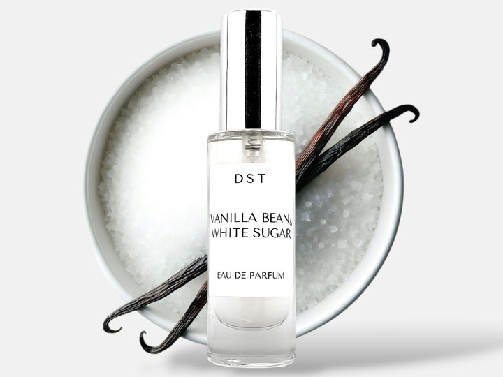 30ml bottle of Vanilla Bean and White Sugar Parfum sitting in front of a large white bowl filled with white sugar with 2 long vanilla beans on top that are lying on top against a white background. 