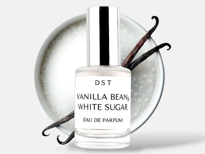 10ml bottle of Vanilla Bean and White Sugar Parfum sitting in front of a large white bowl filled with white sugar with 2 long vanilla beans on top that are lying on top against a white background. 