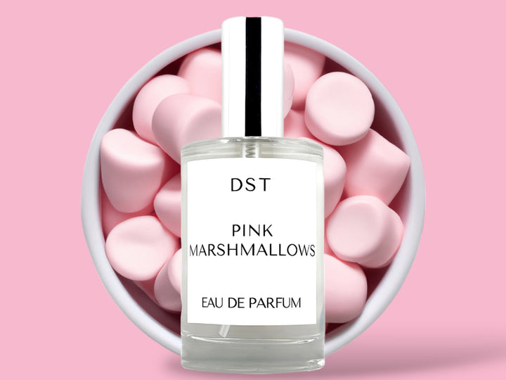 100ML bottle of Pink Marshmallows Eau de Parfum sitting in front of a large white bowl filled with fluffy pink marshmallows against a pastel pink background. 