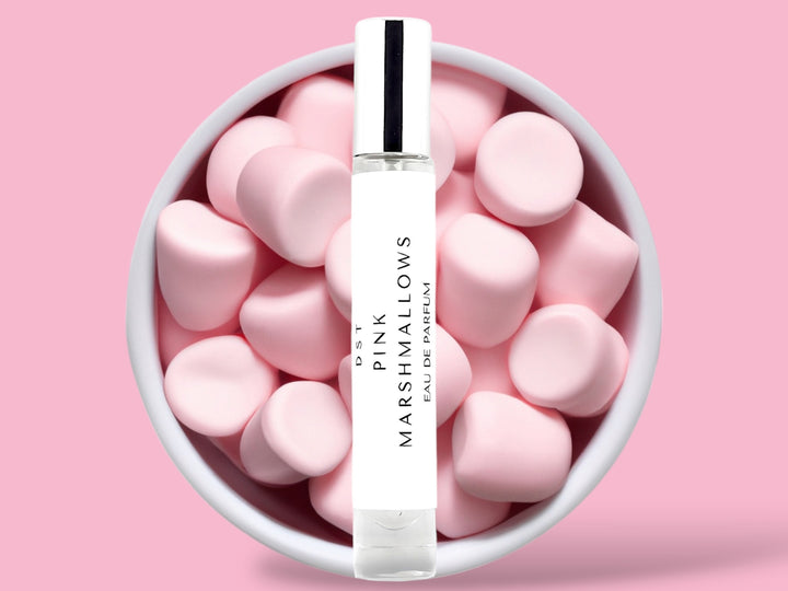 10ML bottle of Pink Marshmallows Eau de Parfum sitting in front of a large white bowl filled with fluffy pink marshmallows against a pastel pink background. 