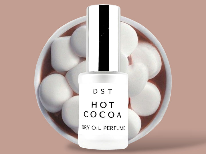 30ML bottle Hot Cocoa dry oil perfume sitting in front of a large white cup of hot chocolate topped with marshmallows against a brown. background.