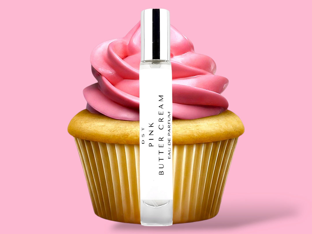 10ml bottle of Pink Butter Cream Parfum sitting in front of a large vanilla cupcake with bright pink frosting against a pink background. 