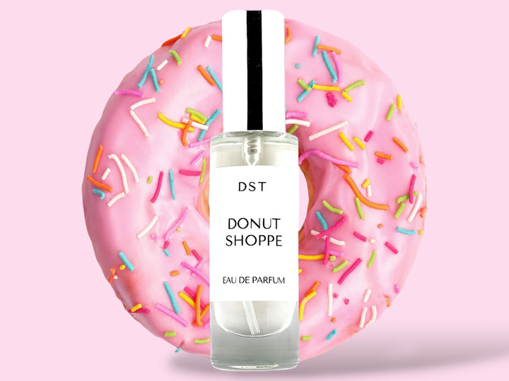 30ML bottle of Donut Shoppe Eau de Parfum sitting in front of a pink Frosted Donut with rainbow sprinkles against a pink background. 