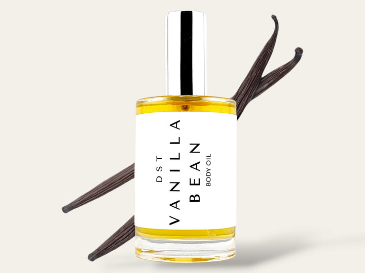 100ml bottle of Vanilla Bean body oil sitting in front of 2 large vanilla beans against an ivory background. 