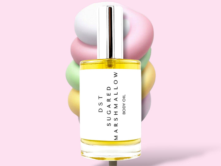 100ML bottle of Sugared Marshmallow Body oil sitting in front of a large pastel multi colored Marshmallow swirl lollipop against a pink background.