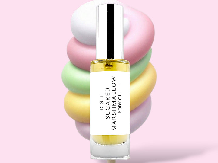 30ML bottle of Sugared Marshmallow Body oil sitting in front of a large pastel multi colored Marshmallow swirl lollipop against a pink background.