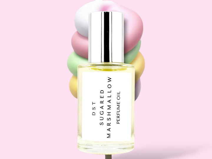 30ML bottle of Sugared Marshmallow perfume oil sitting in front of a large pastel multi colored Marshmallow swirl lollipop against a pink background.