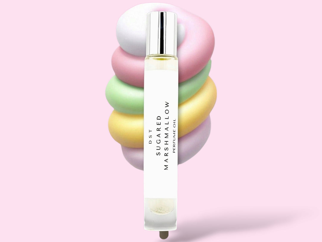 10ML bottle of Sugared Marshmallow perfume oil sitting in front of a large pastel multi colored Marshmallow swirl lollipop against a pink background.