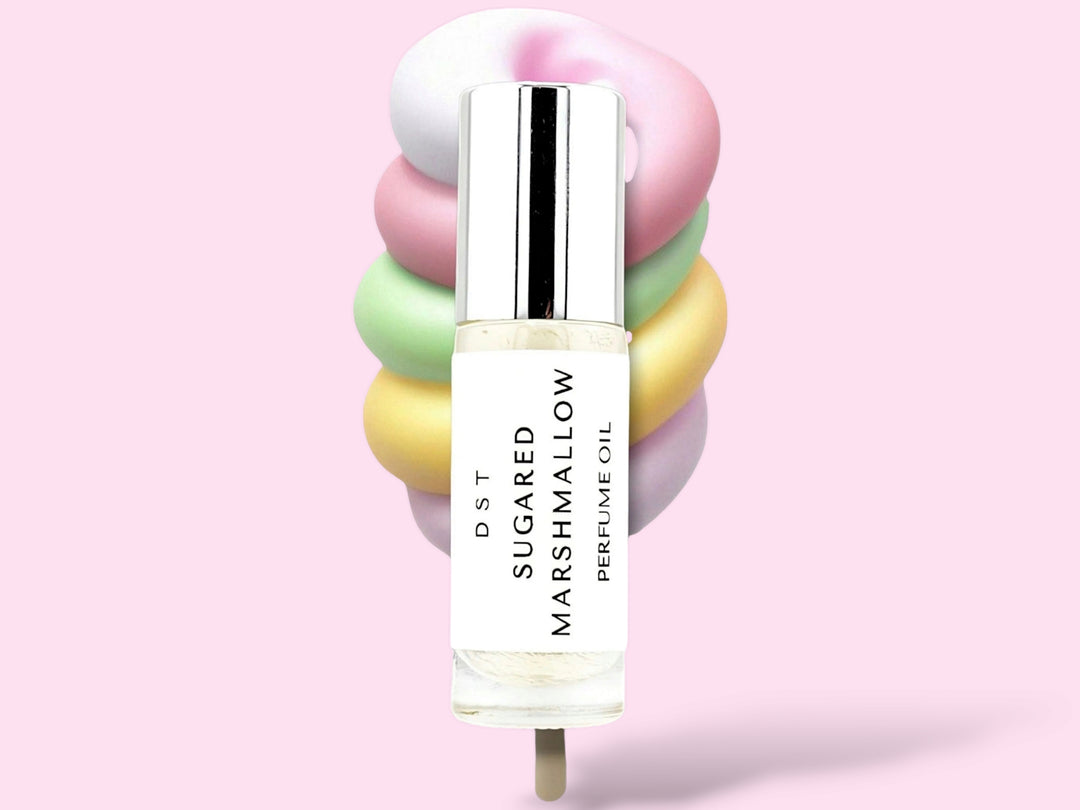 5ML bottle of Sugared Marshmallow perfume oil sitting in front of a large pastel multi colored Marshmallow swirl lollipop against a pink background.