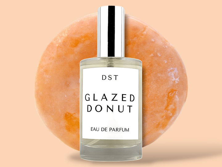 100ml bottle of glazed donut eau de parfum sitting in front of a large glazed donut on a cream colored background