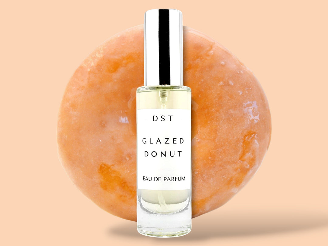 30ml bottle of glazed donut eau de parfum sitting in front of a large glazed donut on a cream colored background.