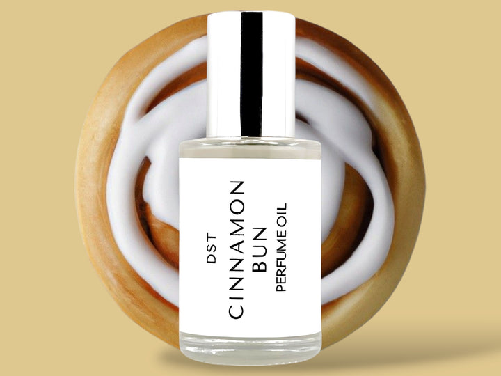 30ML bottle of Cinnamon Bun perfume oil sitting in front of a large Cinnamon Bun with white frosting against a tan background. 