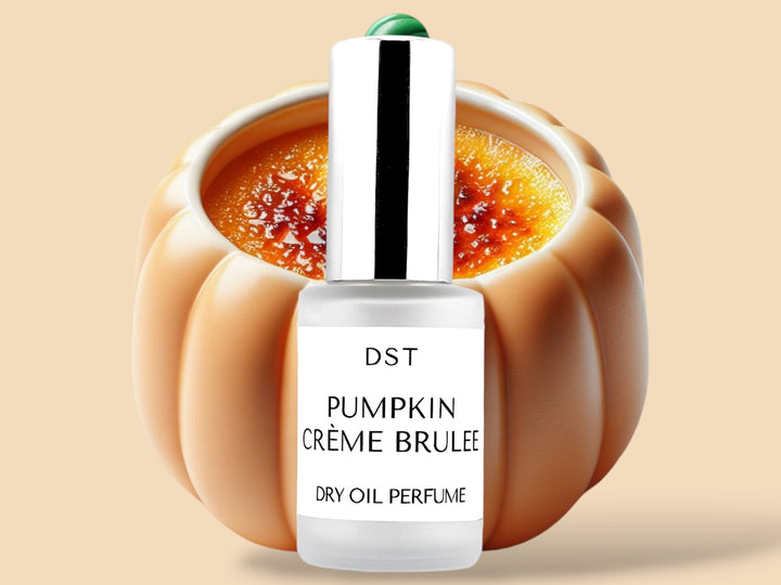 30ML bottle of Pumpkin Creme Brulée Dry Oil Perfume Spray sitting in front of a large ceramic Pumpkin shaped bowl filled with creme brulee against a pastel orange background. 