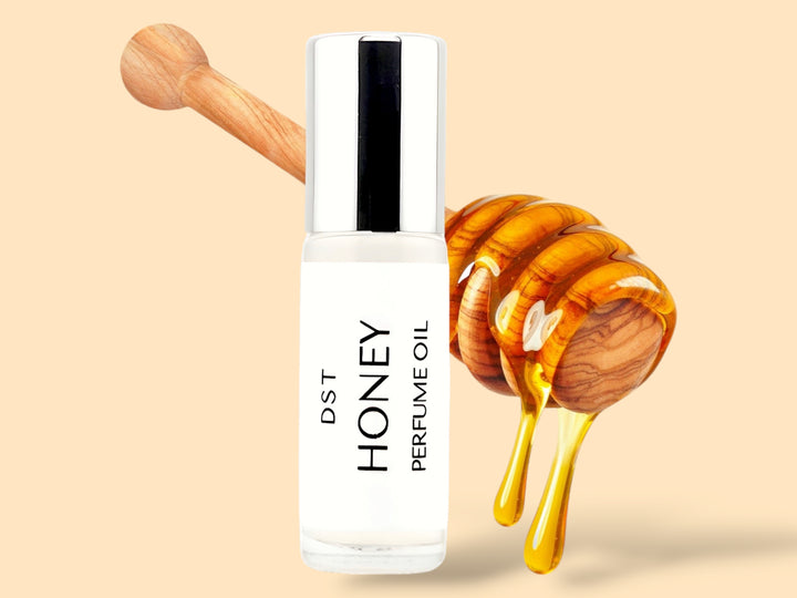 5ML bottle of Honey perfume oil sitting in front of a large wooden honey dipper that is dripping with honey against a tan background. 