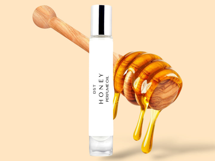 10ML bottle of Honey perfume oil sitting in front of a large wooden honey dipper that is dripping with honey against a tan background. 