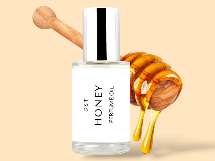 30ML bottle of Honey perfume oil sitting in front of a large wooden honey dipper that is dripping with honey against a tan background. 