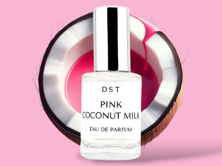 10ml bottle of Pink Coconut Milk Parfum sitting in front of a large opened Coconut that is filled with pink colored Coconut milk against a pink background. 