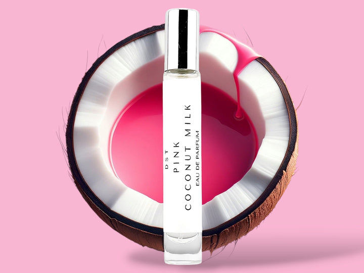 10ml bottle of Pink Coconut Milk Parfum sitting in front of a large opened Coconut that is filled with pink colored Coconut milk against a pink background. 