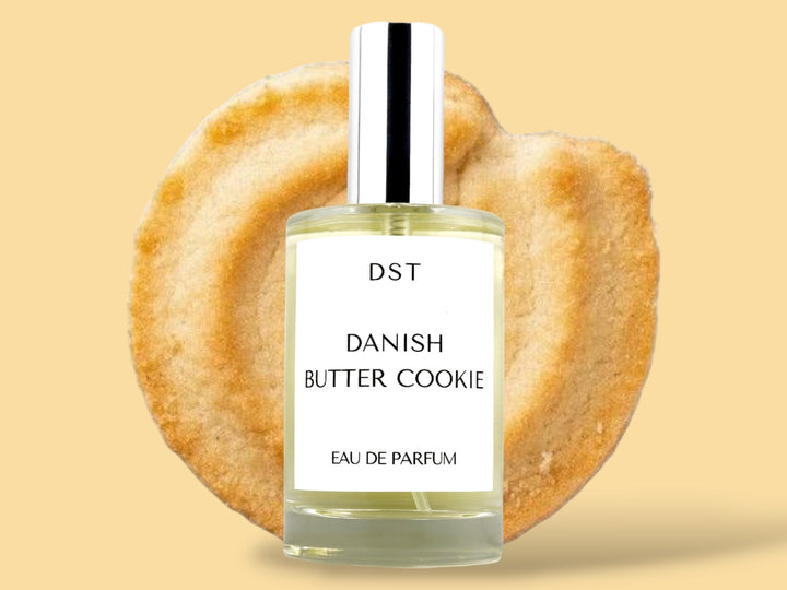 100ML bottle of Danish Butter Cookie Eau de Parfum sitting in front of a large Butter cookie against a pastel yelloe background. 