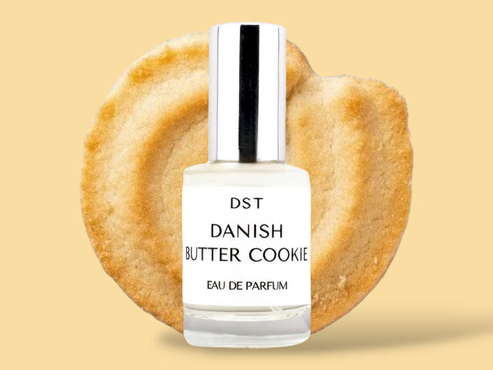 10ML bottle of Danish Butter Cookie Eau de Parfum sitting in front of a large Butter cookie against a pastel yelloe background. 