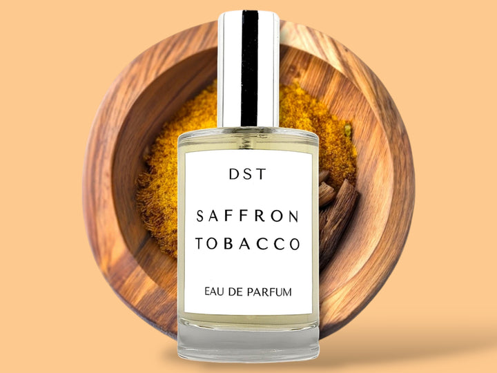 100 ML bottle of saffron tobacco Eau de parfum sitting in front of a wooden bowl filled with saffron against an orange background.