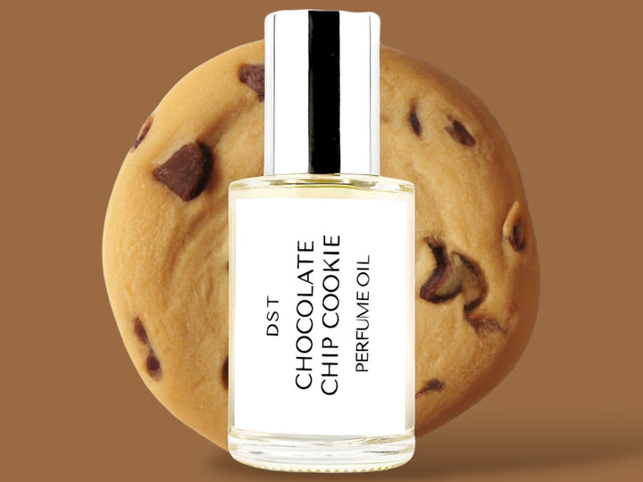 30ml bottle of Chocolate Chip Cookie Perfume Oil sitting in front  of a large Chocolate chip cookie against a brown background. 