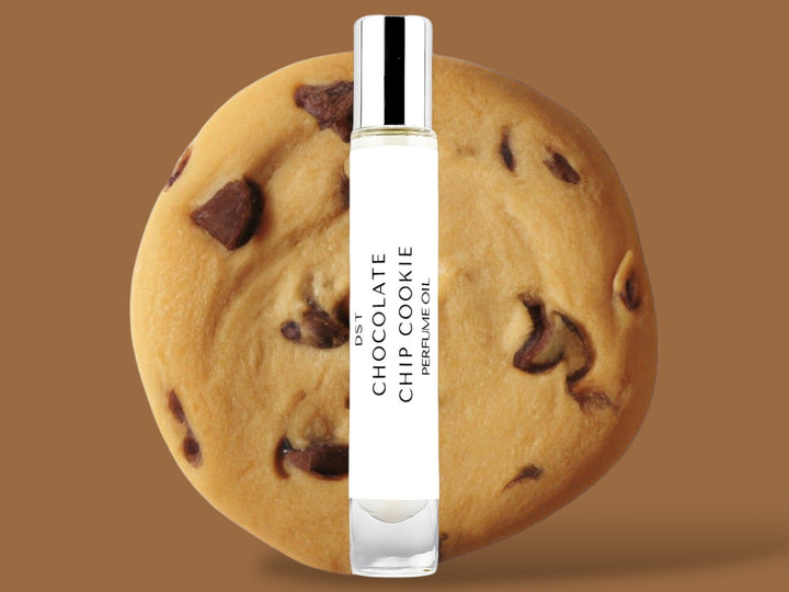 10ml bottle of Chocolate Chip Cookie Perfume Oil sitting in front  of a large Chocolate chip cookie against a brown background. 