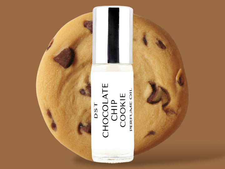 5ml bottle of Chocolate Chip Cookie Perfume Oil sitting in front  of a large Chocolate chip cookie against a brown background. 