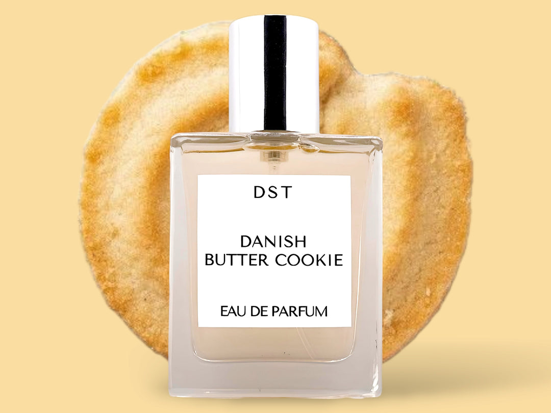 50ML bottle of Danish Butter Cookie Eau de Parfum sitting in front of a large Butter cookie against a pastel yelloe background. 