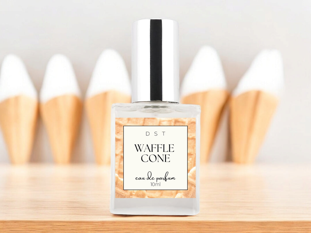 10ml bottle of Waffle Cone Eau de Parfum sitting on wood counter top with 4 Vanilla ice cream cones in the light grey background.