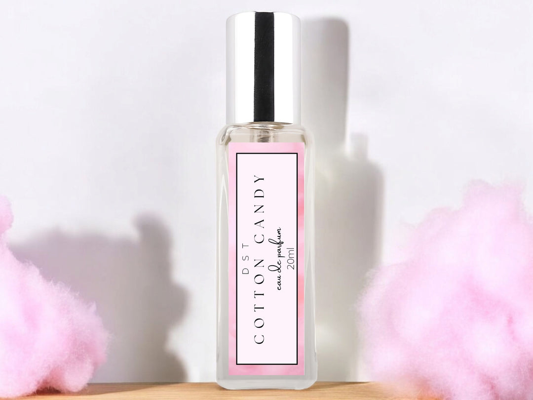 20ml bottle of Cotton Candy Parfum sitting on a wood counter top with puffs of cotton candy in the white background. 