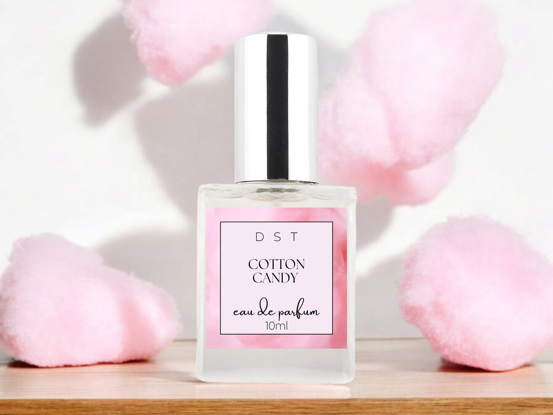 10ml bottle of Cotton Candy Parfum sitting on a wood counter top with puffs of cotton candy in the white background. 