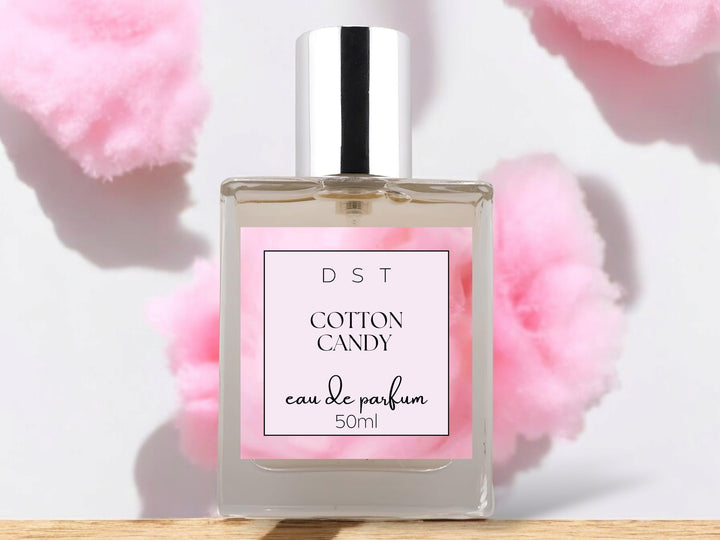 50ml bottle of Cotton Candy Parfum sitting on a wood counter top with puffs of cotton candy in the white background. 