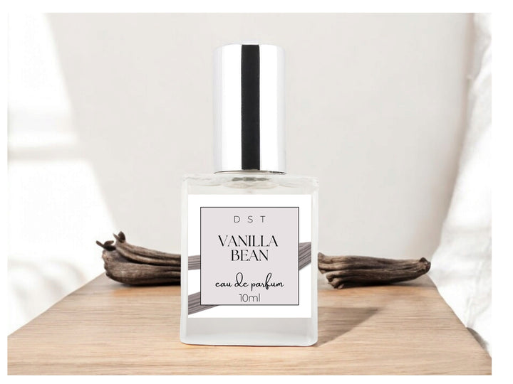 10ml bottle of Vanilla Bean Parfum sitting on a white countertop with a couple of vanilla beans in the light grey background. 