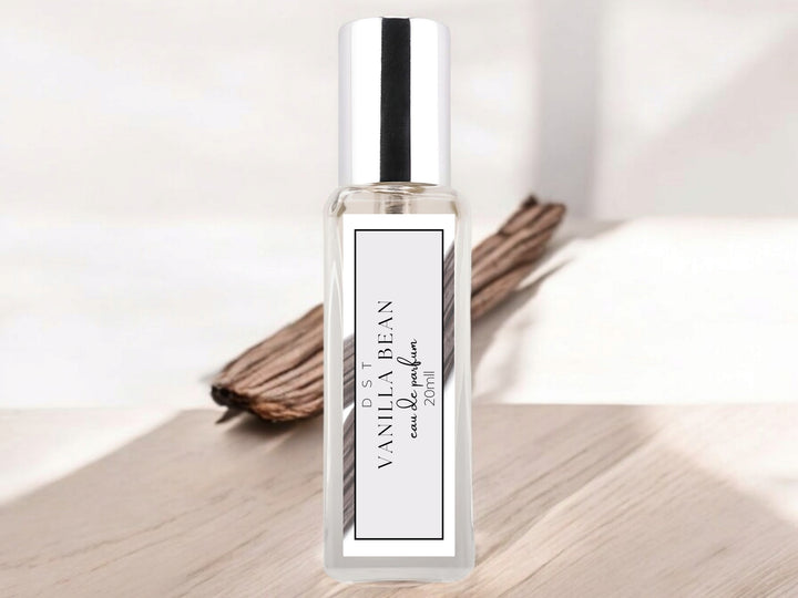 20ml bottle of Vanilla Bean Parfum sitting on a wood countertop with a couple of vanilla beans in the light grey background. 