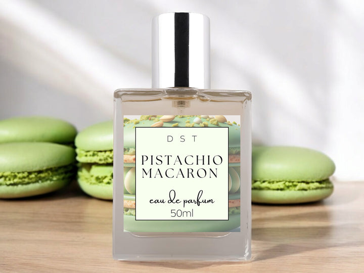 50ml bottle of Pistachio Macaroon Eau de Parfum sitting on wood counter top with white background and green macarons surrounding the bottle.