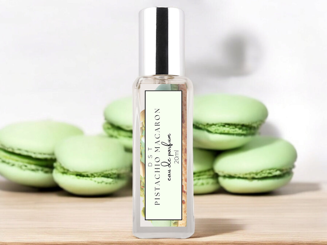 20ml bottle of Pistachio Macaroon Eau de Parfum sitting on wood counter top with white background and green macarons surrounding the bottle.