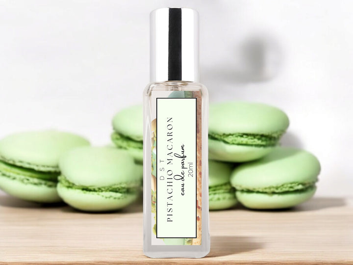 20ml bottle of Pistachio Macaroon Eau de Parfum sitting on wood counter top with white background and green macarons surrounding the bottle.