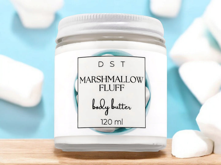 4oz jar of Marshmallow Fluff Body Butter sitting on wood counter top with light blue background and white marshmallows.