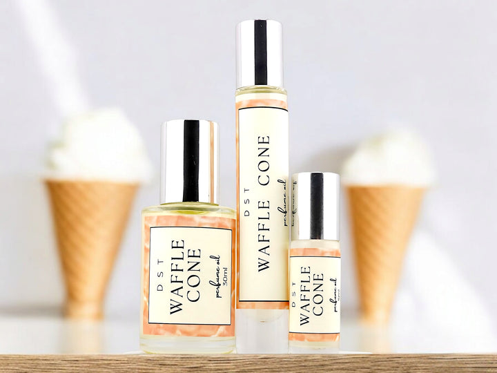 5, 10, and 30ml bottles of waffle cone perfume oil sitting on wood counter top with white background and 2 waffle cones filled with vanilla ice cream.