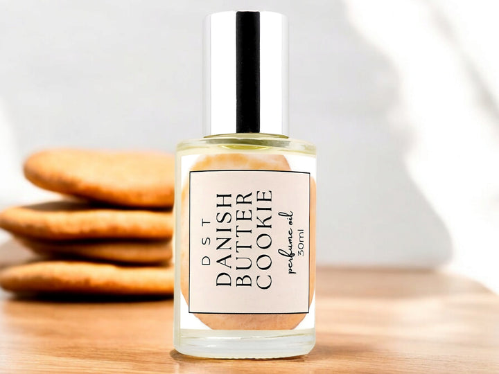 30ML bottle of Danish Butter Cookie perfume oil sitting on a wood countertop with butter cookies stacked against a white background.