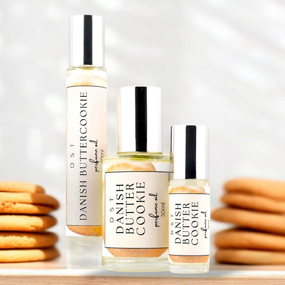 5, 10, and 30ML bottle of Danish Butter Cookie perfume oil sitting on a wood countertop with butter cookies stacked against a white background.