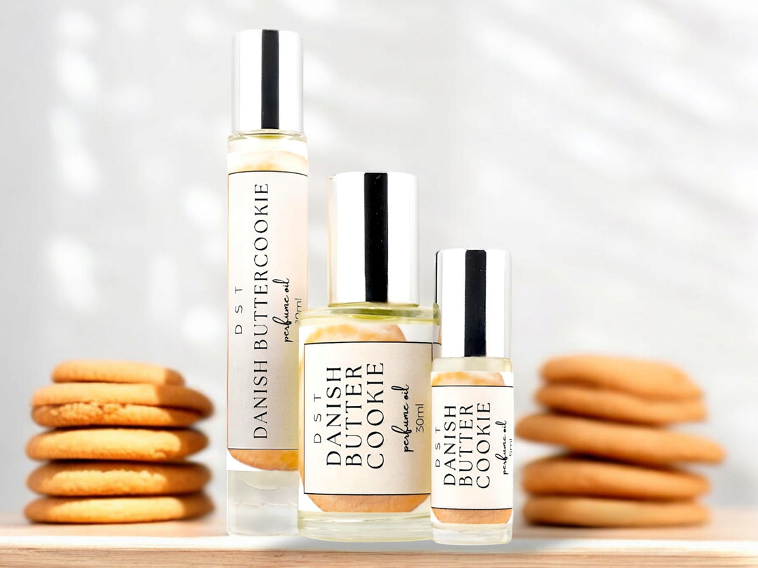 5, 10, and 30ML bottle of Danish Butter Cookie perfume oil sitting on a wood countertop with butter cookies stacked against a white background.