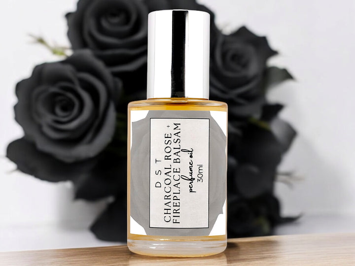 30ml bottle of Charcoal Rose and Fireplace Balsam Perfume oil sitting in front of a large black rose on against a light grey background. 