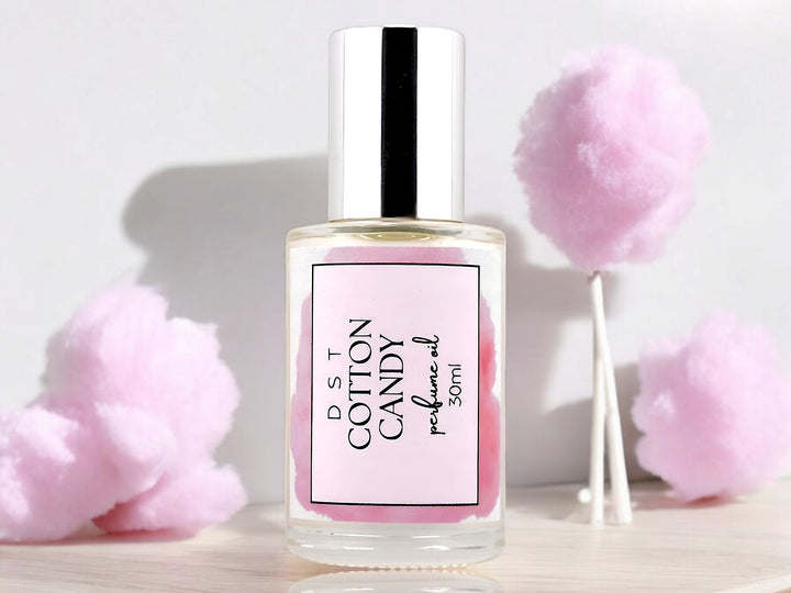 30ml bottle of Cotton Candy perfume oil sitting  wood counter top with fluffy pink cotton candy in the white shadowy background.