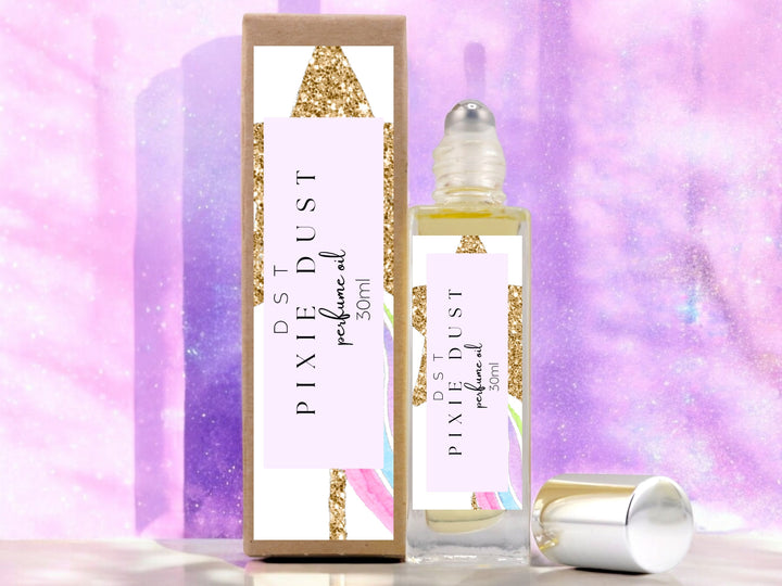 30ml bottle of Pixie Dust perfume oil and the box it is packaged in sitting on wood countertop with pastel purple glittery background.