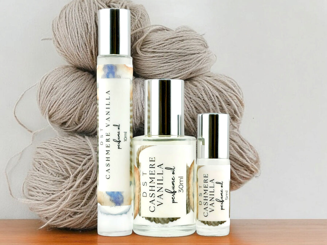 5, 10, and 30ml bottles of Cashmere Vanilla perfume oil sitting in front of balls of grey yarn against a light gray background.