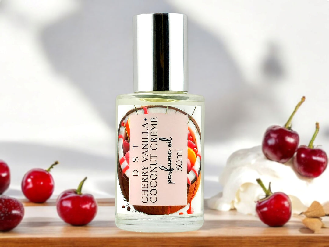 30ml bottle of Cherry Vanilla and Coconut Cream perfume oil sitting on wood countertop with bright red cherries and whipped crem in the white background.